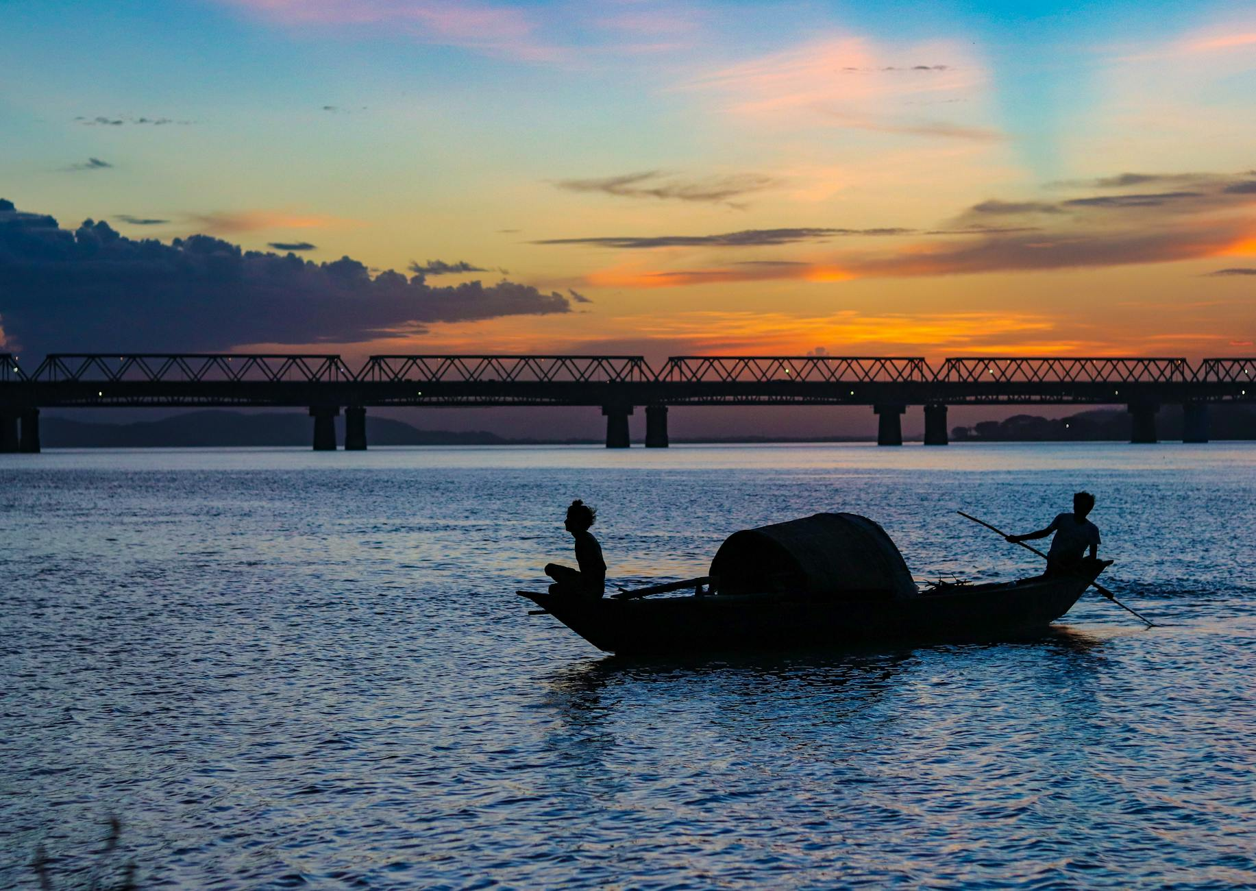 Brahmaputra river sunset golden fisherman boat silhouette Assam